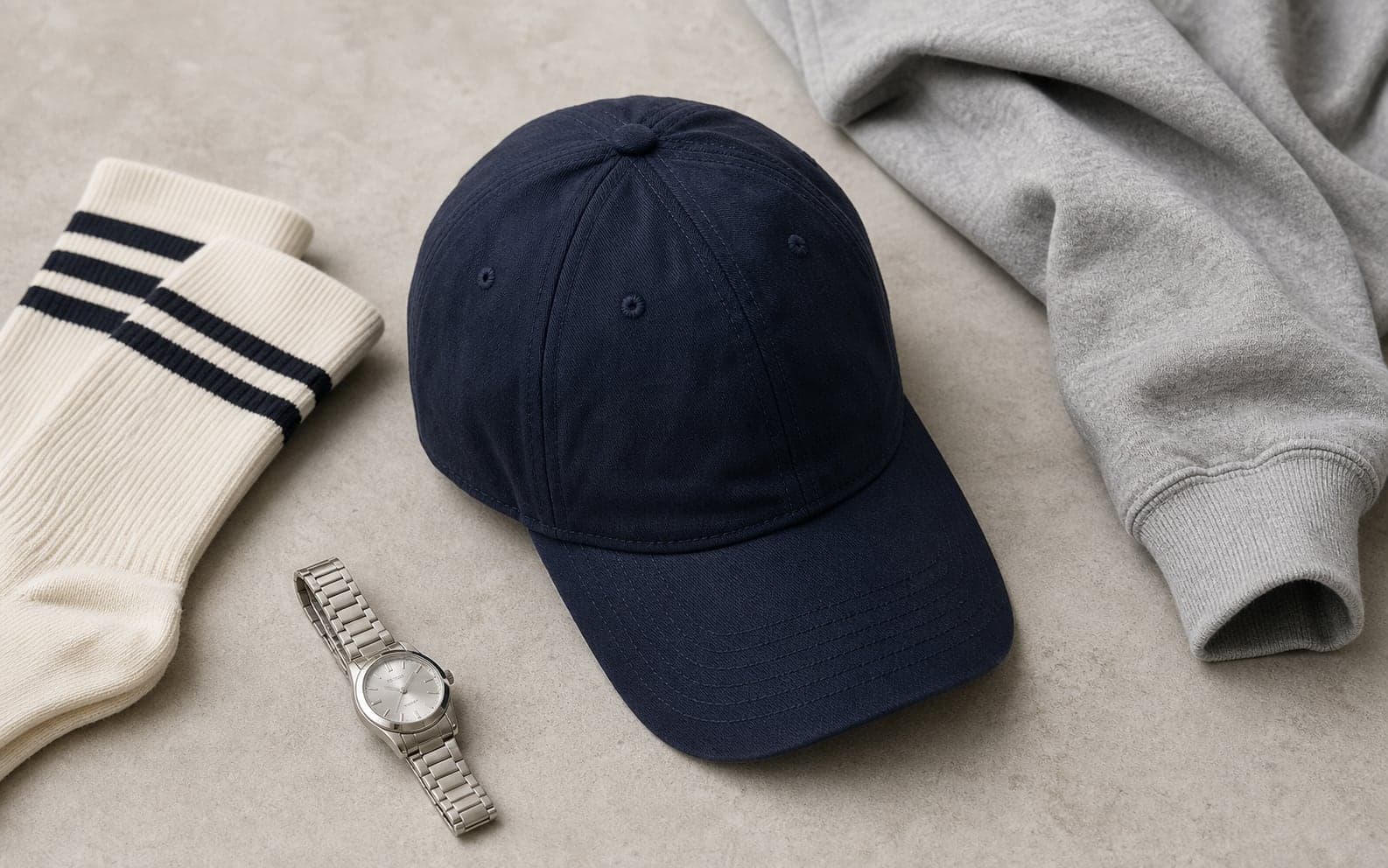 A navy baseball cap arranged with tube socks, a silver watch, and a sweatshirt sleeve.