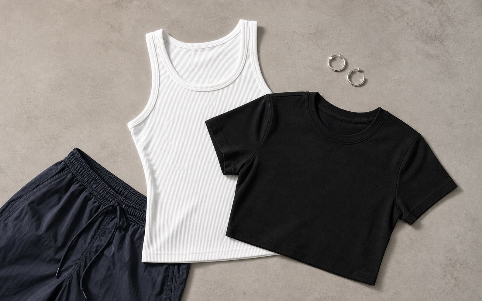 A white ribbed tank and black baby tee arranged with track pants and small hoop earrings.
