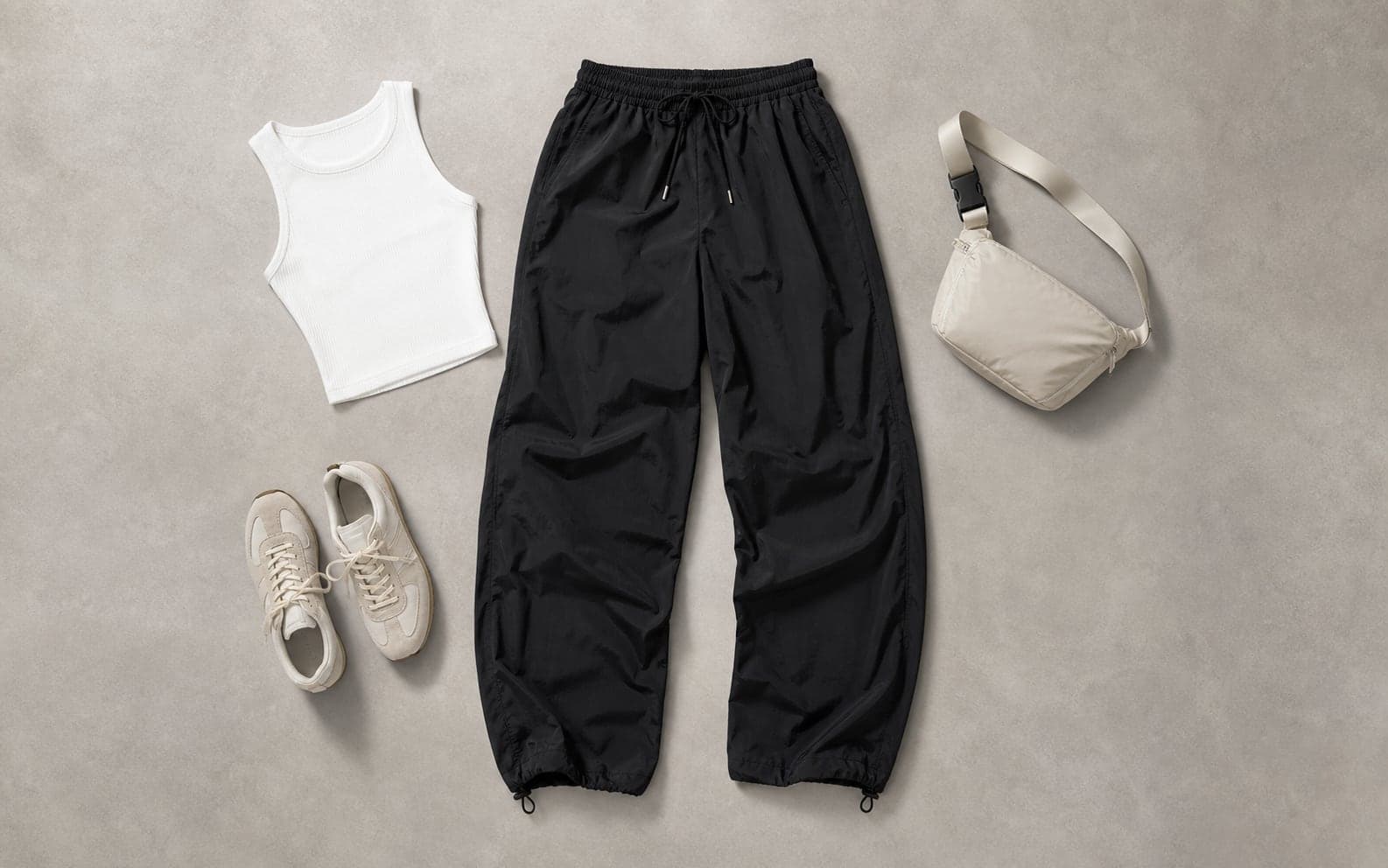 Loose black nylon athletic pants arranged with a cropped white tank and low-profile sneakers.