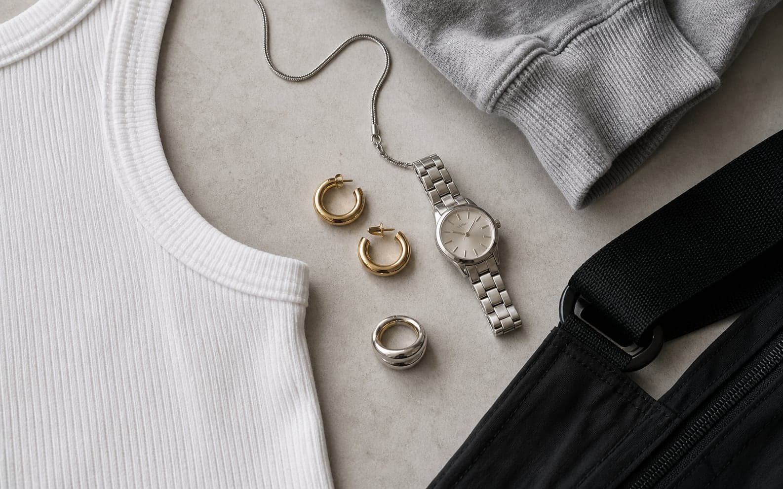 Small hoops, a slim watch, a simple chain, and a ring arranged with ribbed cotton and nylon textures.