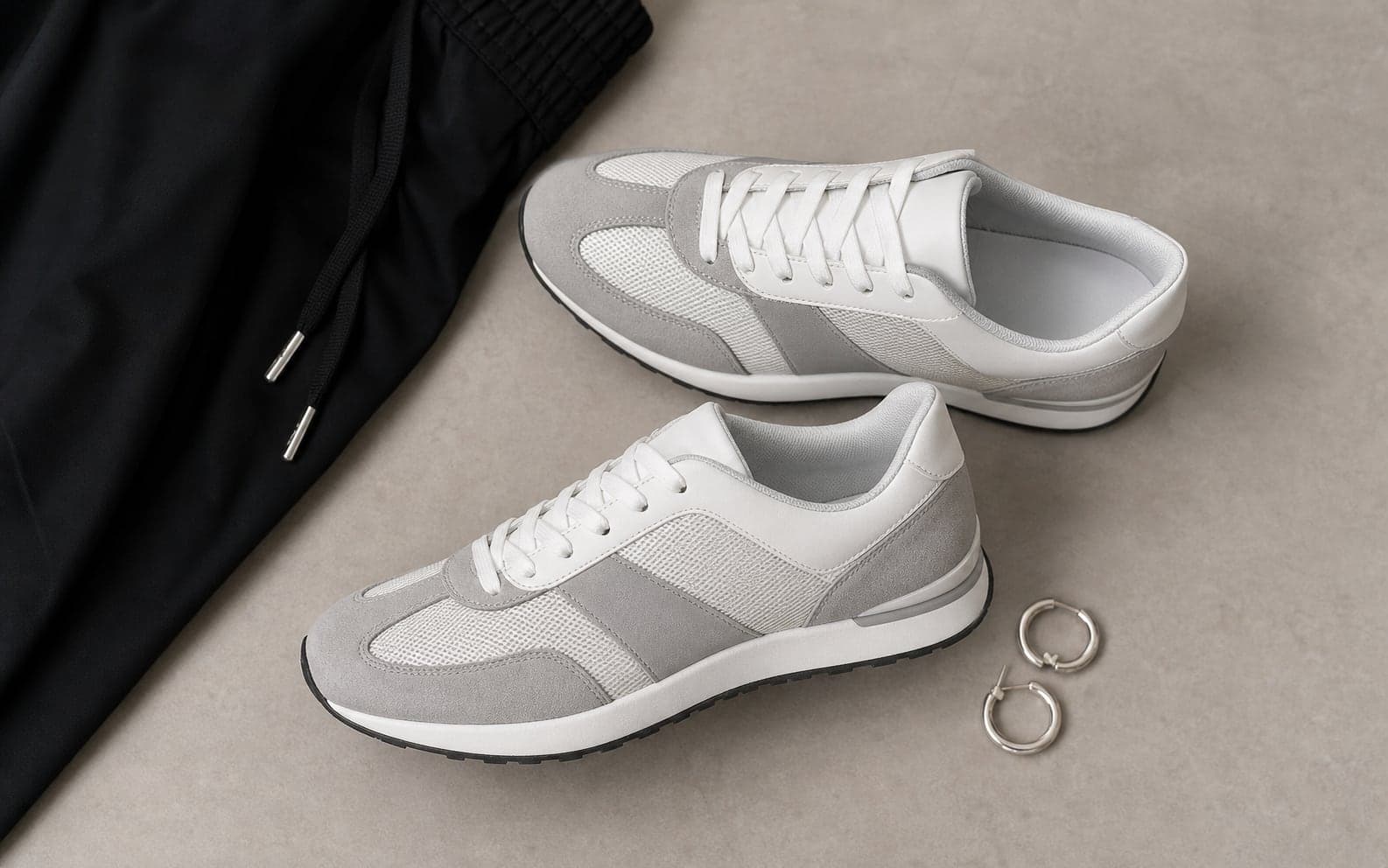 Low-profile white and gray sleek trainers arranged with a black track pant hem.