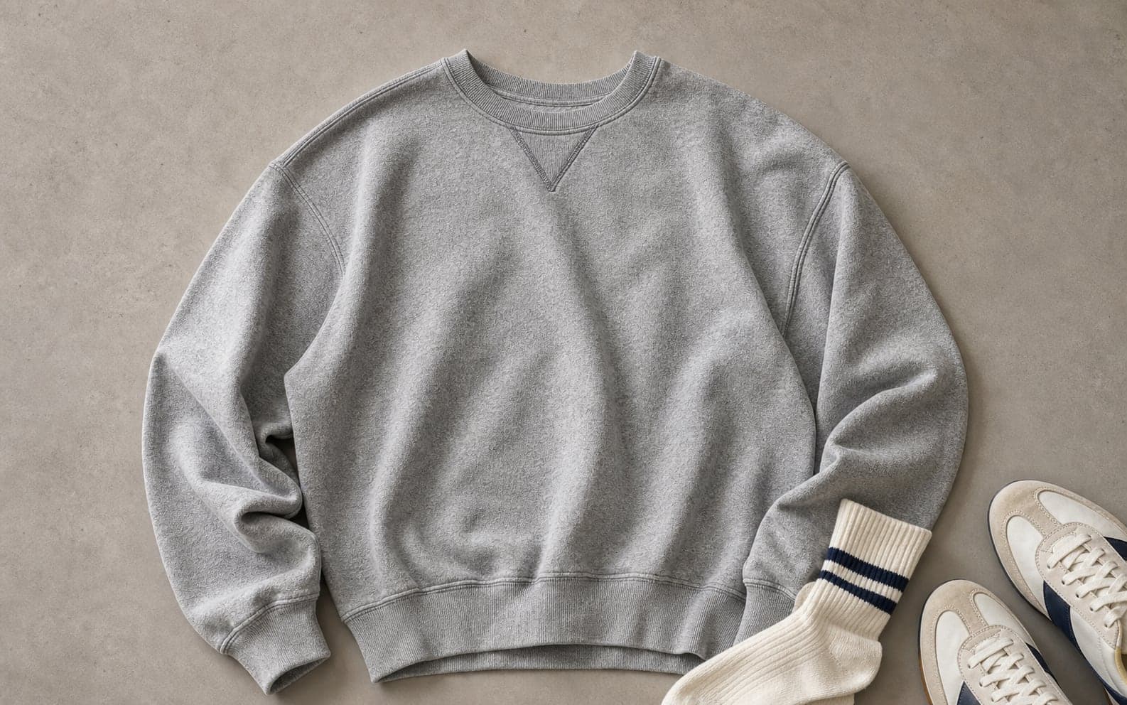 A heather gray vintage-style crewneck sweatshirt arranged with tube socks and retro sneakers.