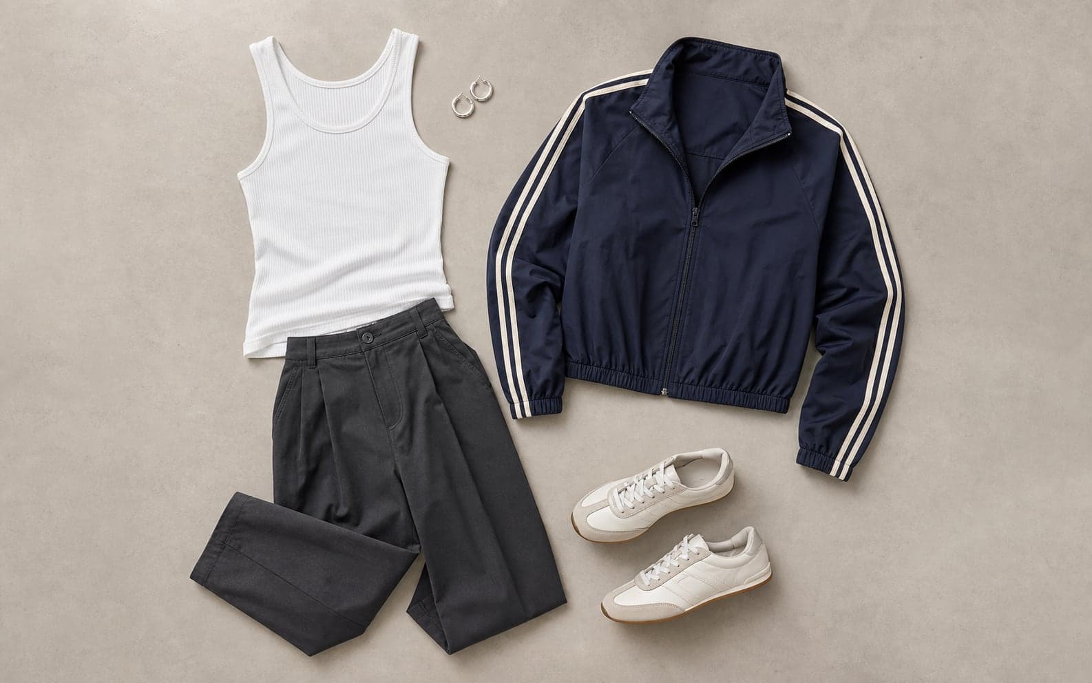 A complete outfit with a ribbed tank, relaxed charcoal trousers, cropped track jacket, sleek trainers, and small hoops.