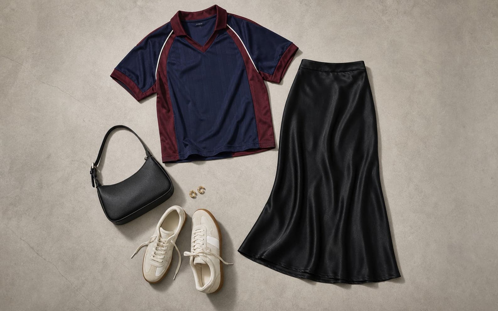 A complete outfit with a navy and burgundy soccer jersey, black satin midi skirt, low-profile sneakers, compact shoulder bag, and gold hoops.