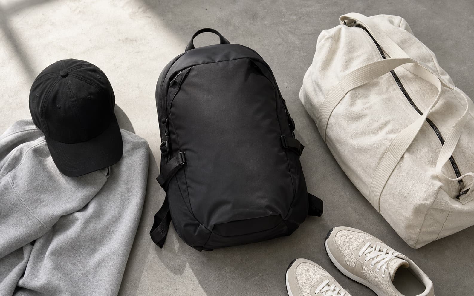 A black cap, matte nylon technical backpack, and clean gym bag styled with athleisure pieces.
