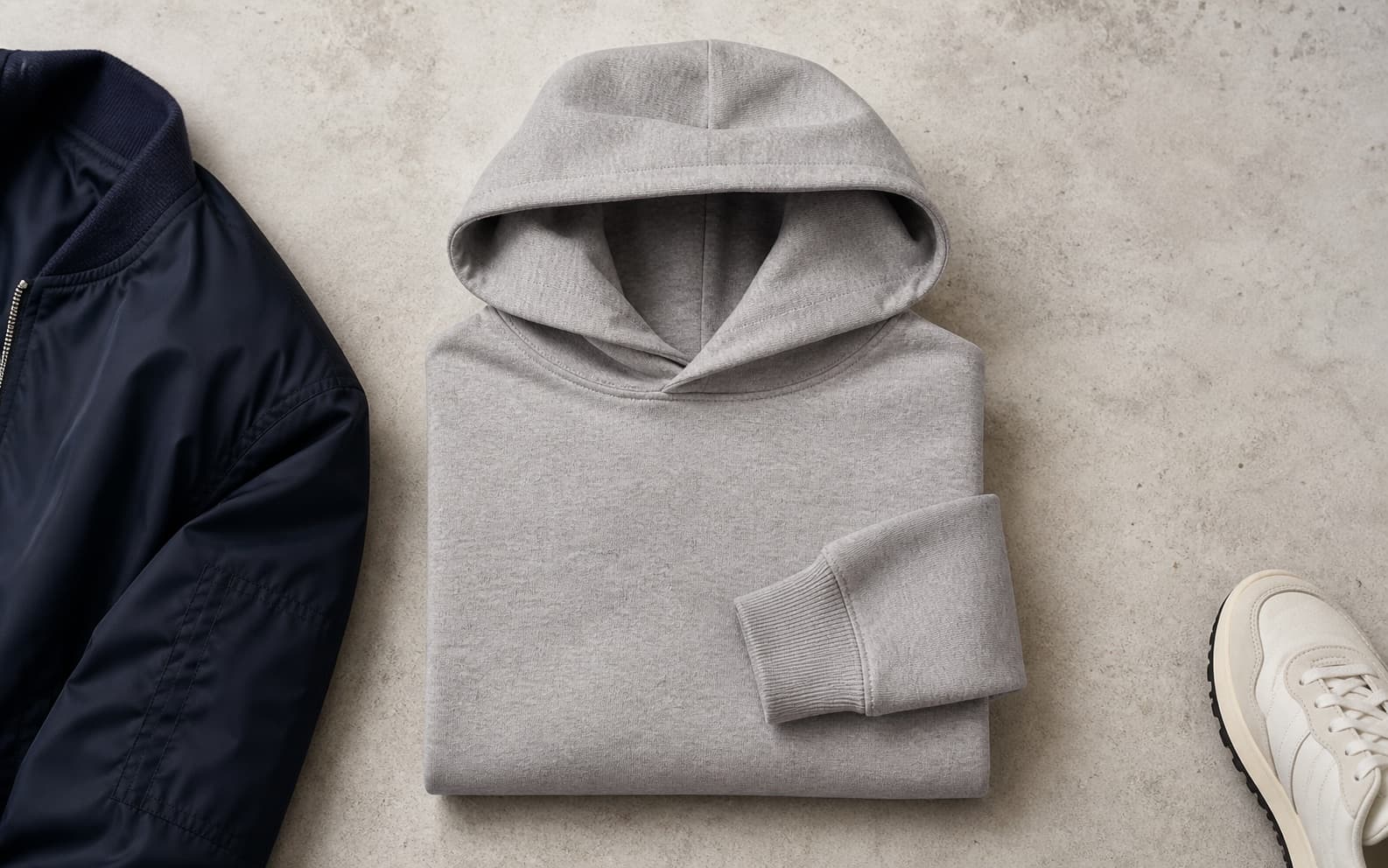 A structured heather gray hoodie folded on a neutral concrete surface.