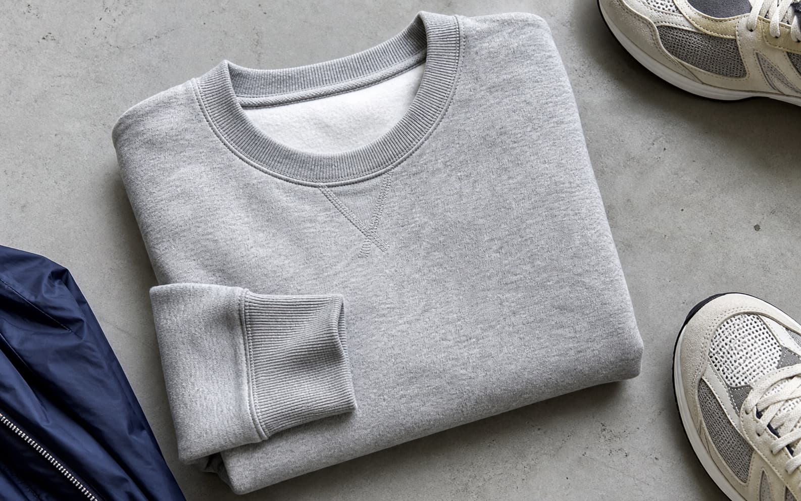 A folded heather gray crewneck sweatshirt with cream sneakers at the edge of the frame.