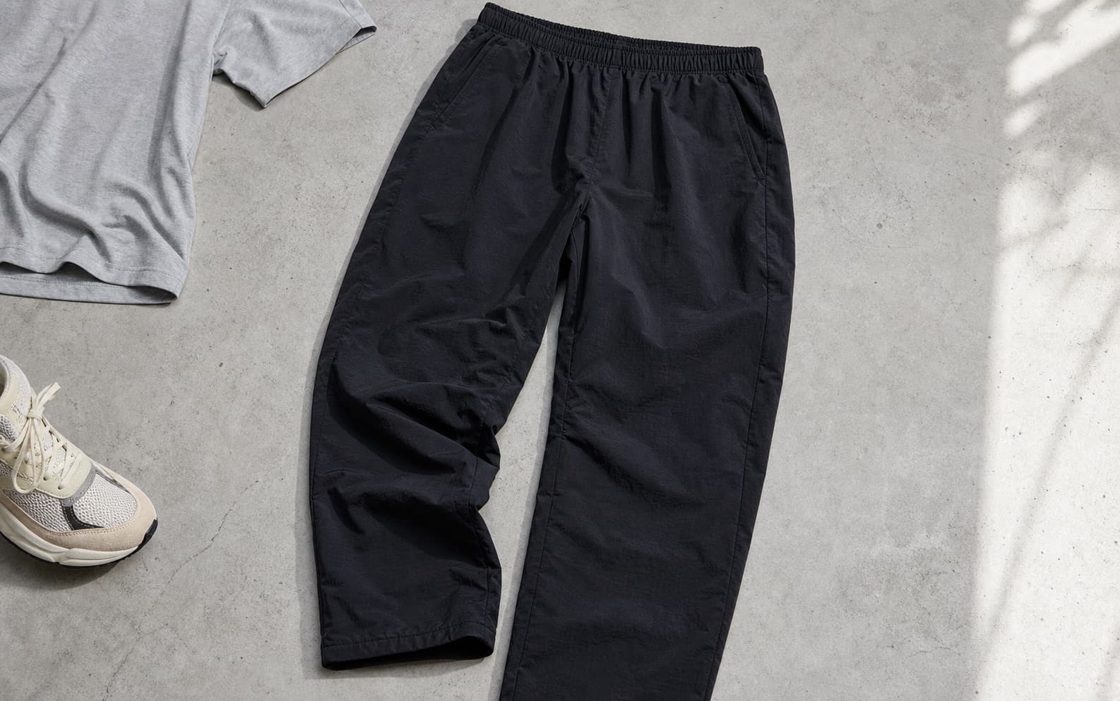 Relaxed black nylon pants laid beside a gray T-shirt and cream sneakers.