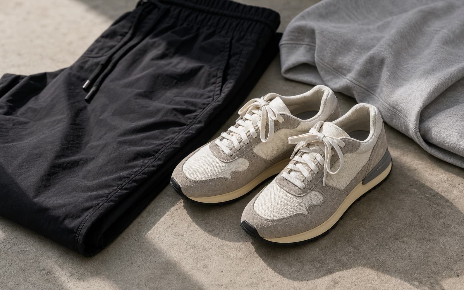 Cream and gray suede and mesh retro runners beside black nylon pants.