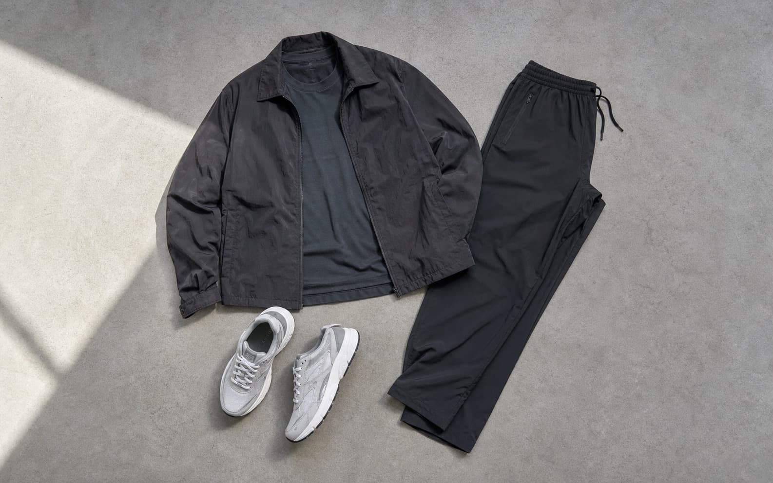 A dark performance tee, nylon overshirt, straight training pants, and clean runners arranged as an outfit.