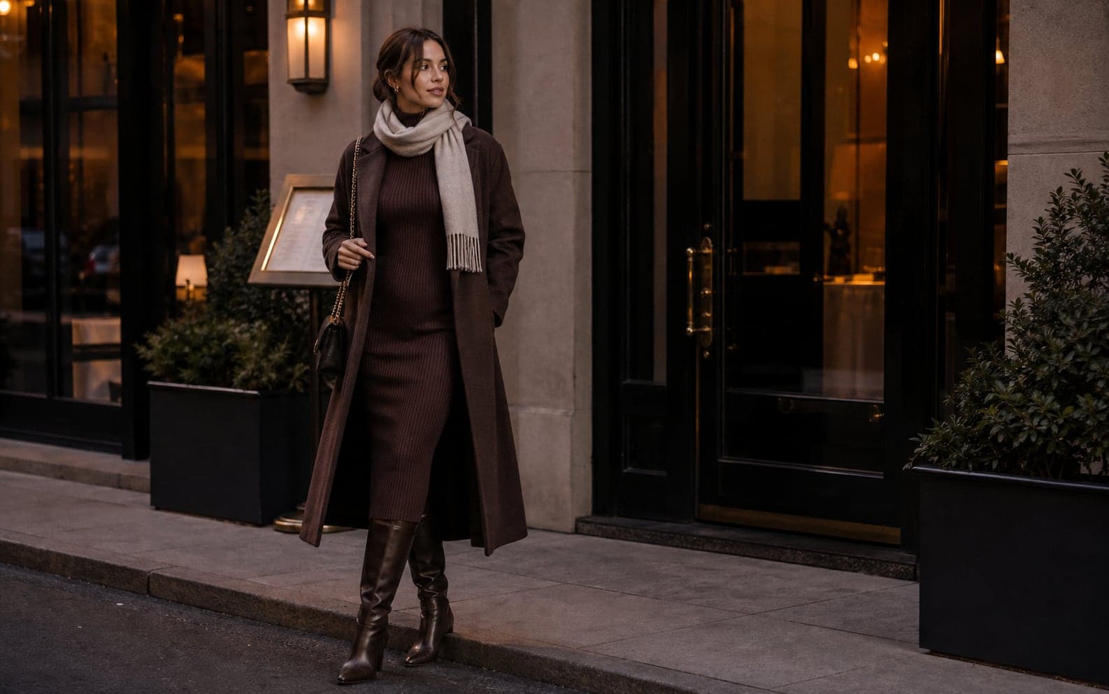 A woman wearing a dark knit dress, black tights, leather jacket, and heeled boots in a polished winter setting.