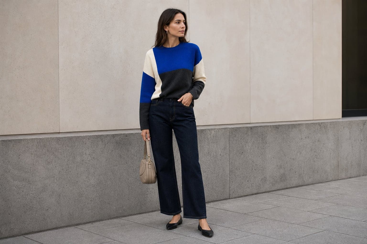 A woman wearing a cobalt, ivory, and charcoal color-blocked knit with dark denim and a neutral bag.