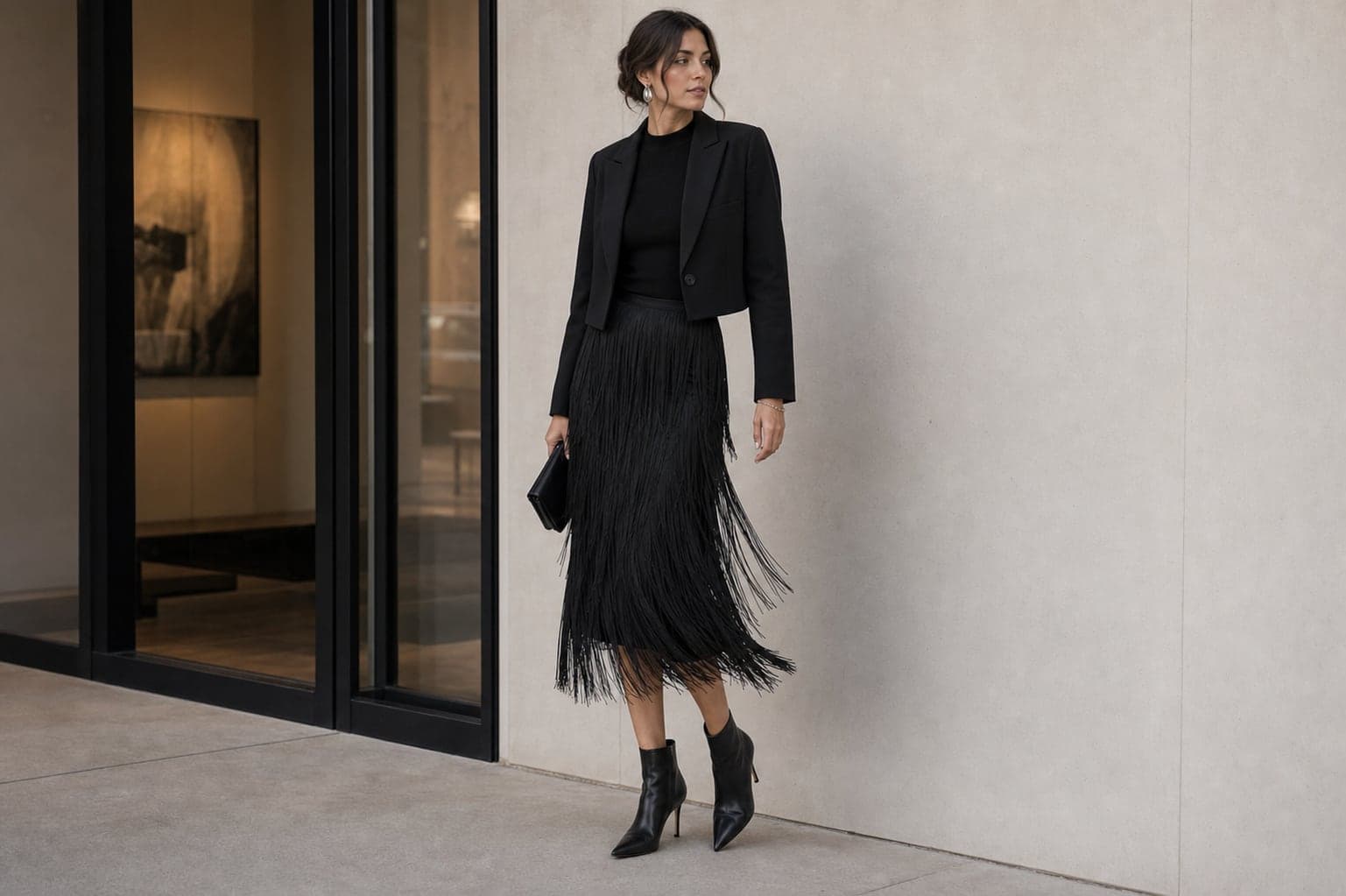 A black fringe midi skirt with a fitted black high-neck knit, cropped jacket, and heeled ankle boots.