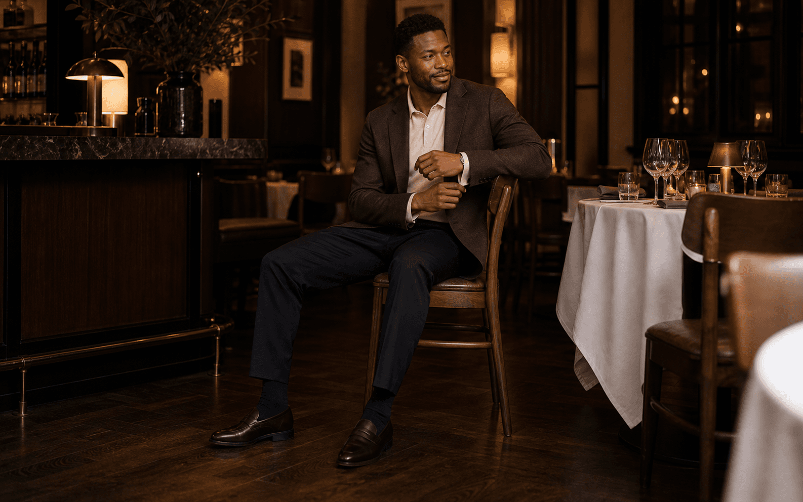 A man near an upscale restaurant wearing an unstructured blazer, cream top, dark trousers, and loafers.
