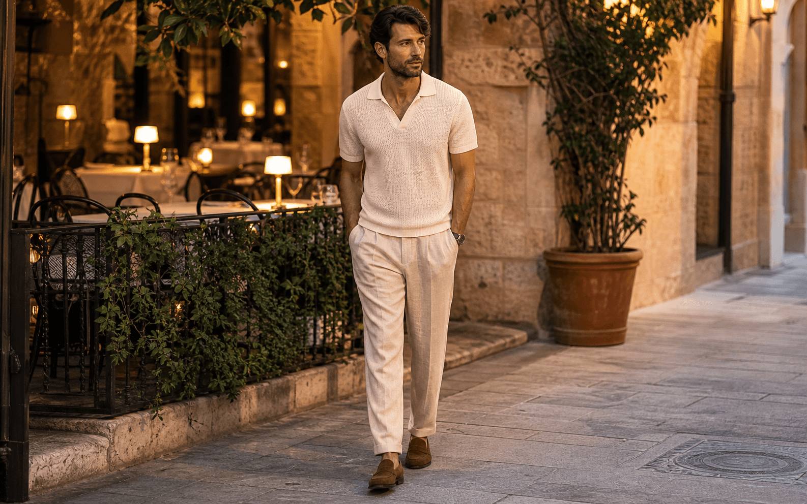 A man on a summer city patio wearing an ecru knit polo, linen trousers, and brown suede loafers.