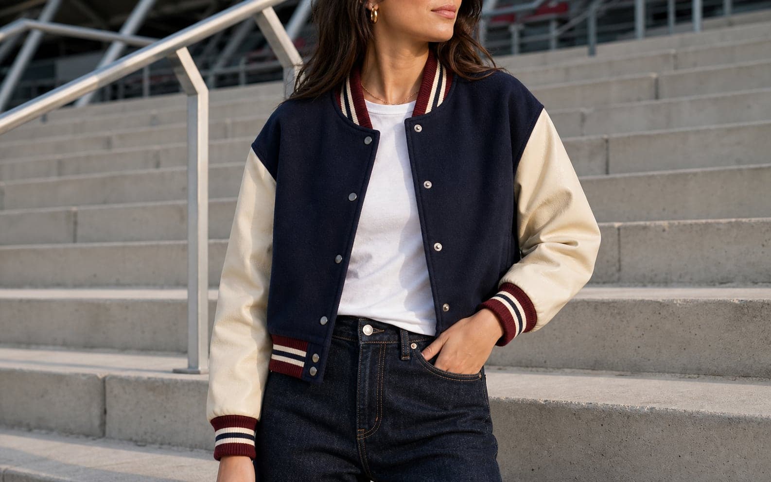 A cropped navy varsity jacket with cream sleeves and burgundy rib trim styled over a white tee and dark denim.