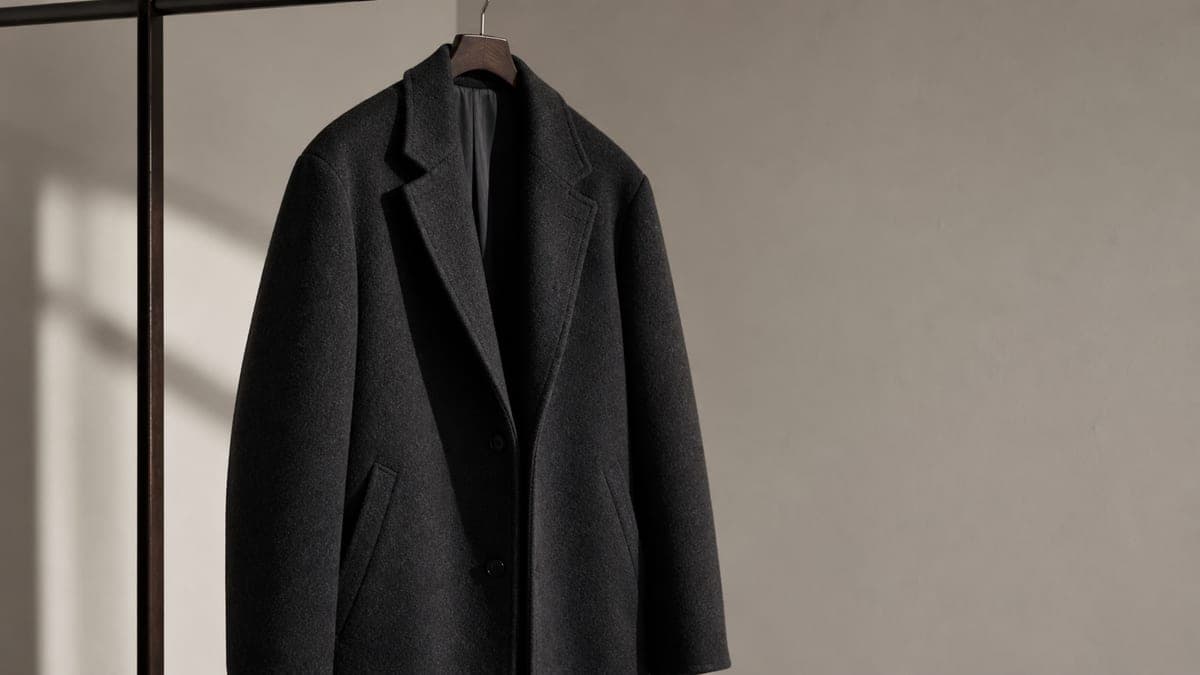 Dark wool coat hanging against a neutral wall.
