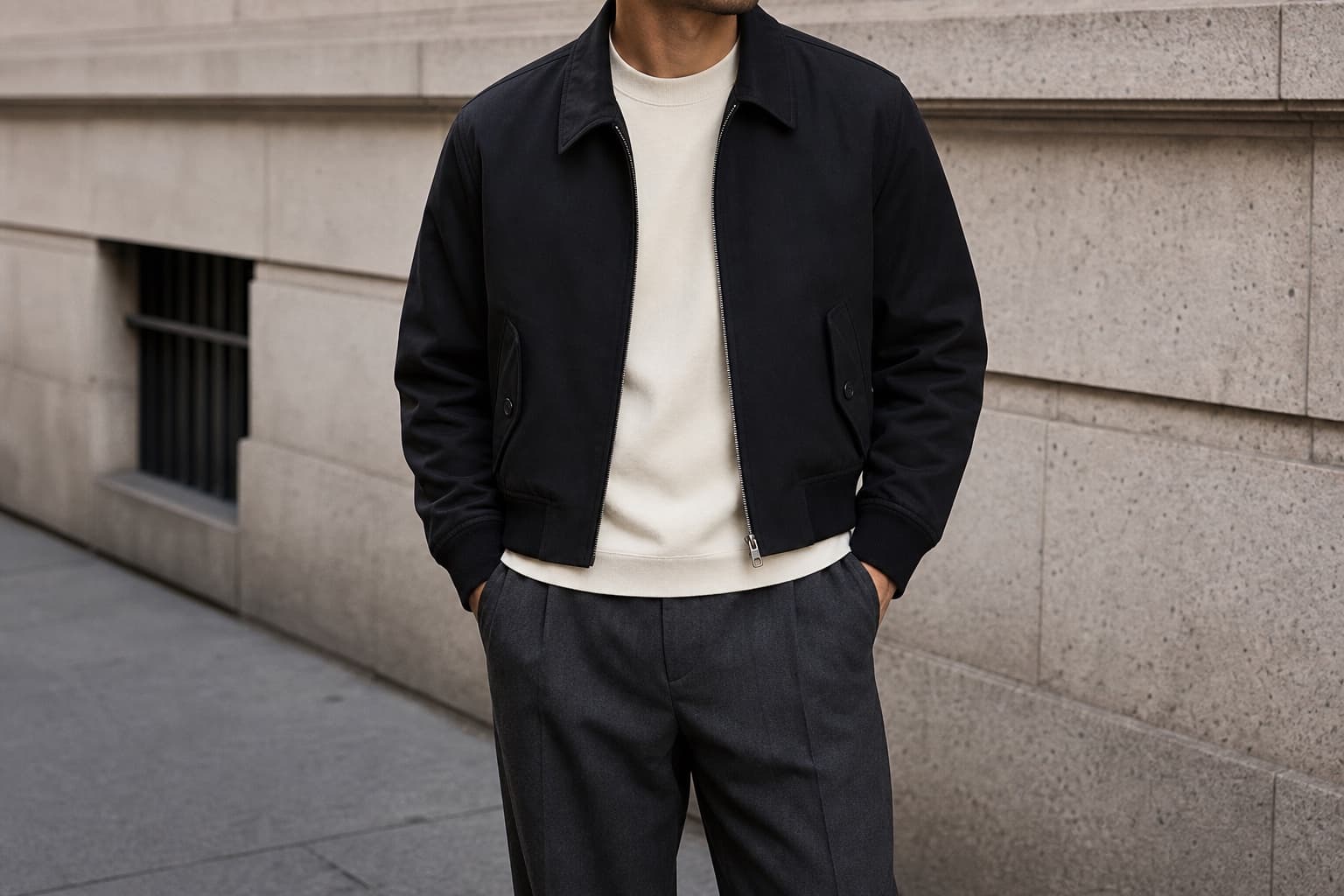 A cropped black bomber jacket worn over a cream tee with relaxed charcoal trousers.