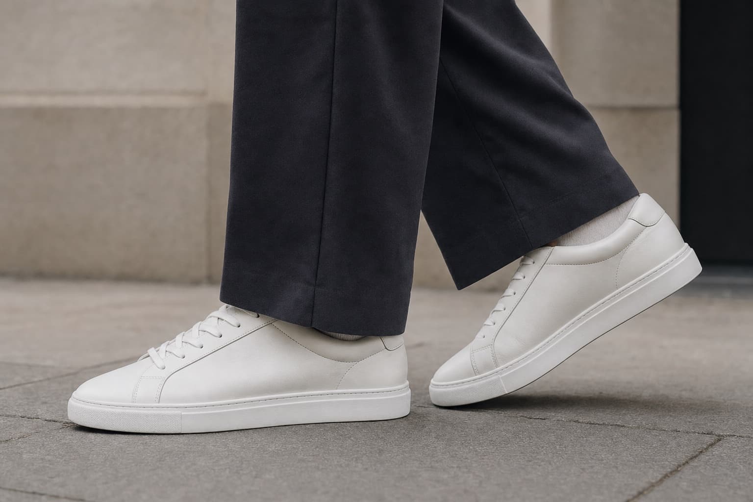 Plain off-white leather sneakers worn with relaxed charcoal trousers.