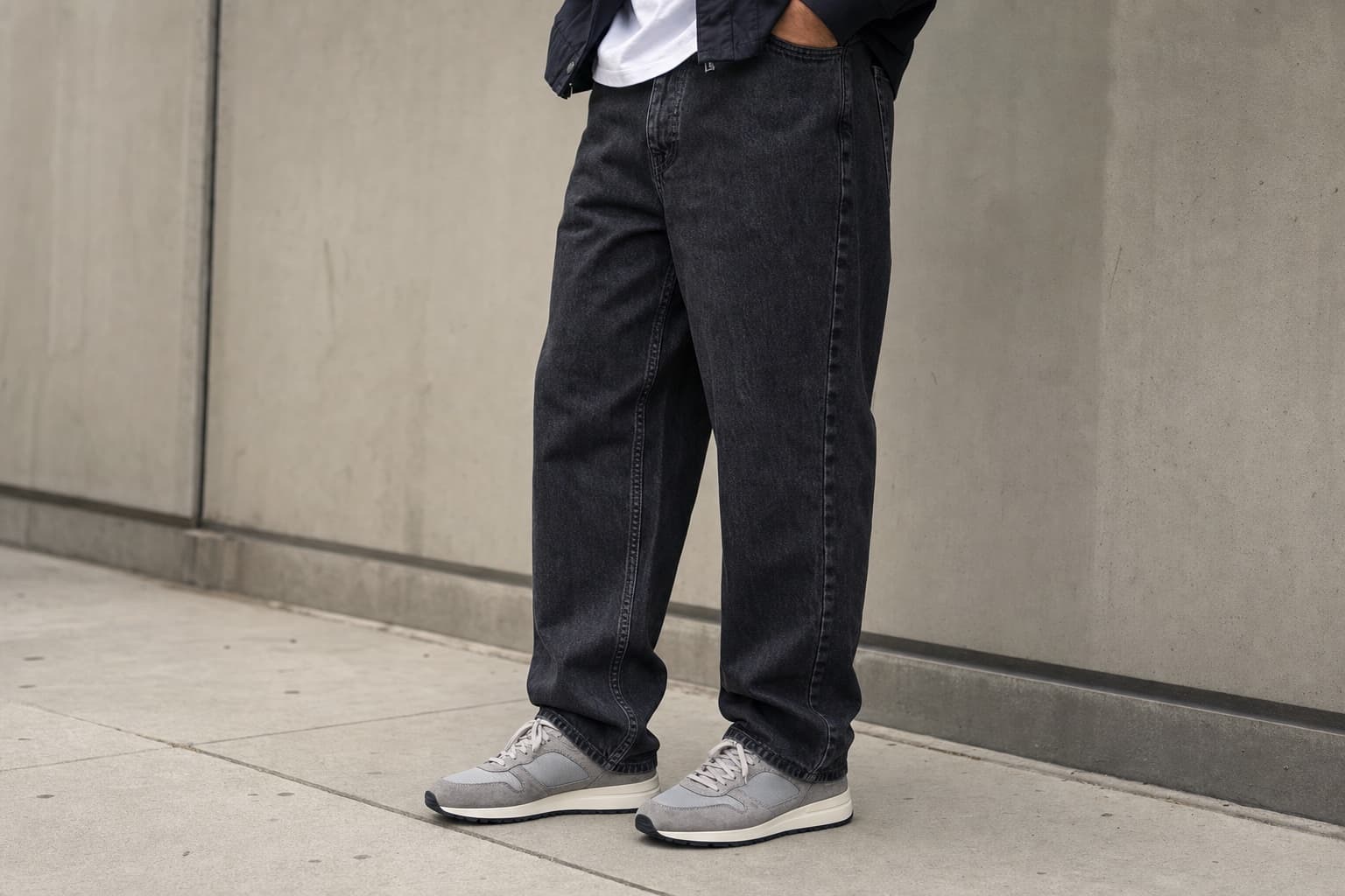Washed black relaxed straight jeans with a clean hem break over gray retro-style sneakers.