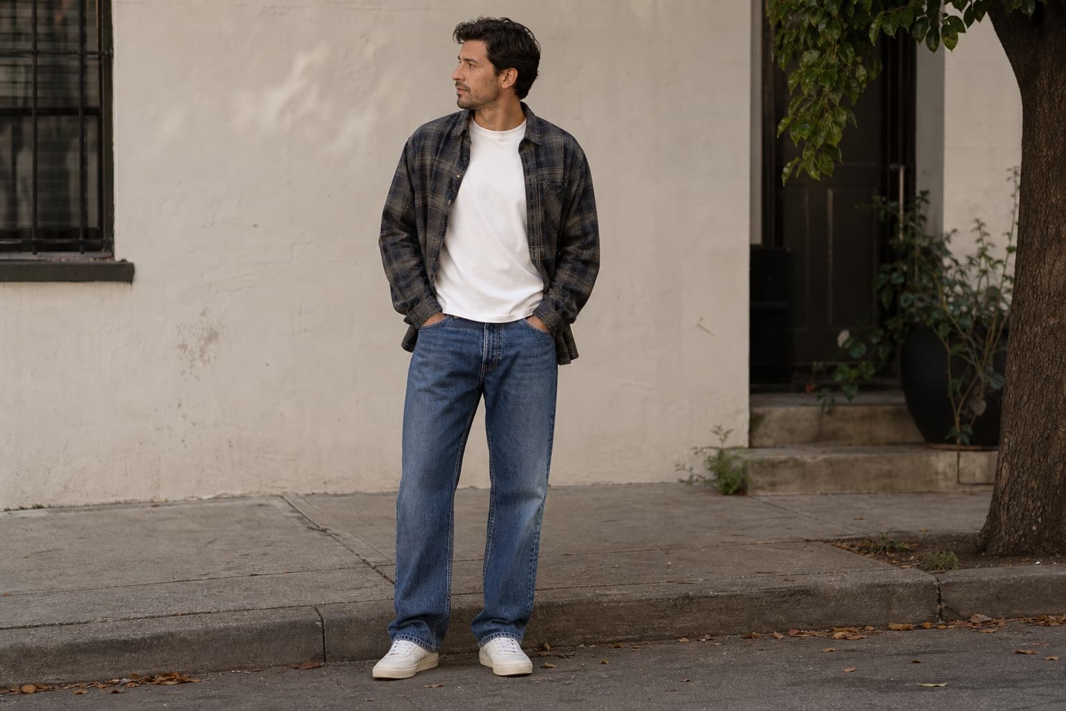 A man wearing a white tee, open muted flannel, straight blue jeans, and clean sneakers.