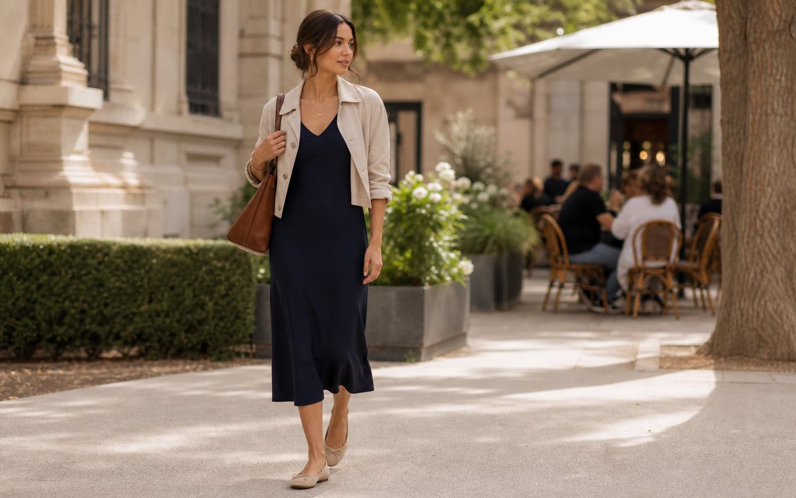 A woman in daylight wearing a midi dress, cropped jacket, low-profile shoes, and simple jewelry.