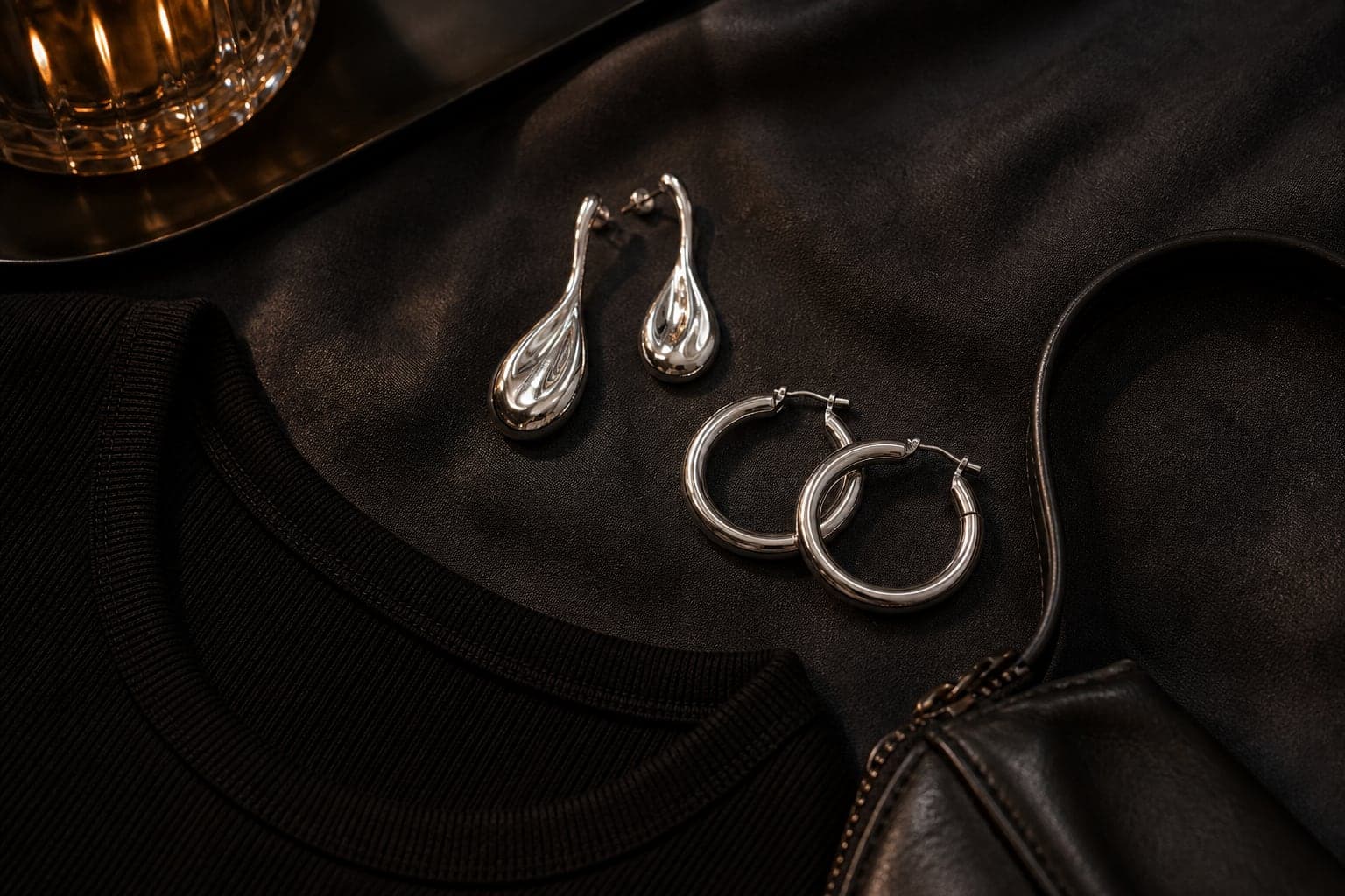 Sculptural silver earrings arranged beside a black neckline and compact evening bag.