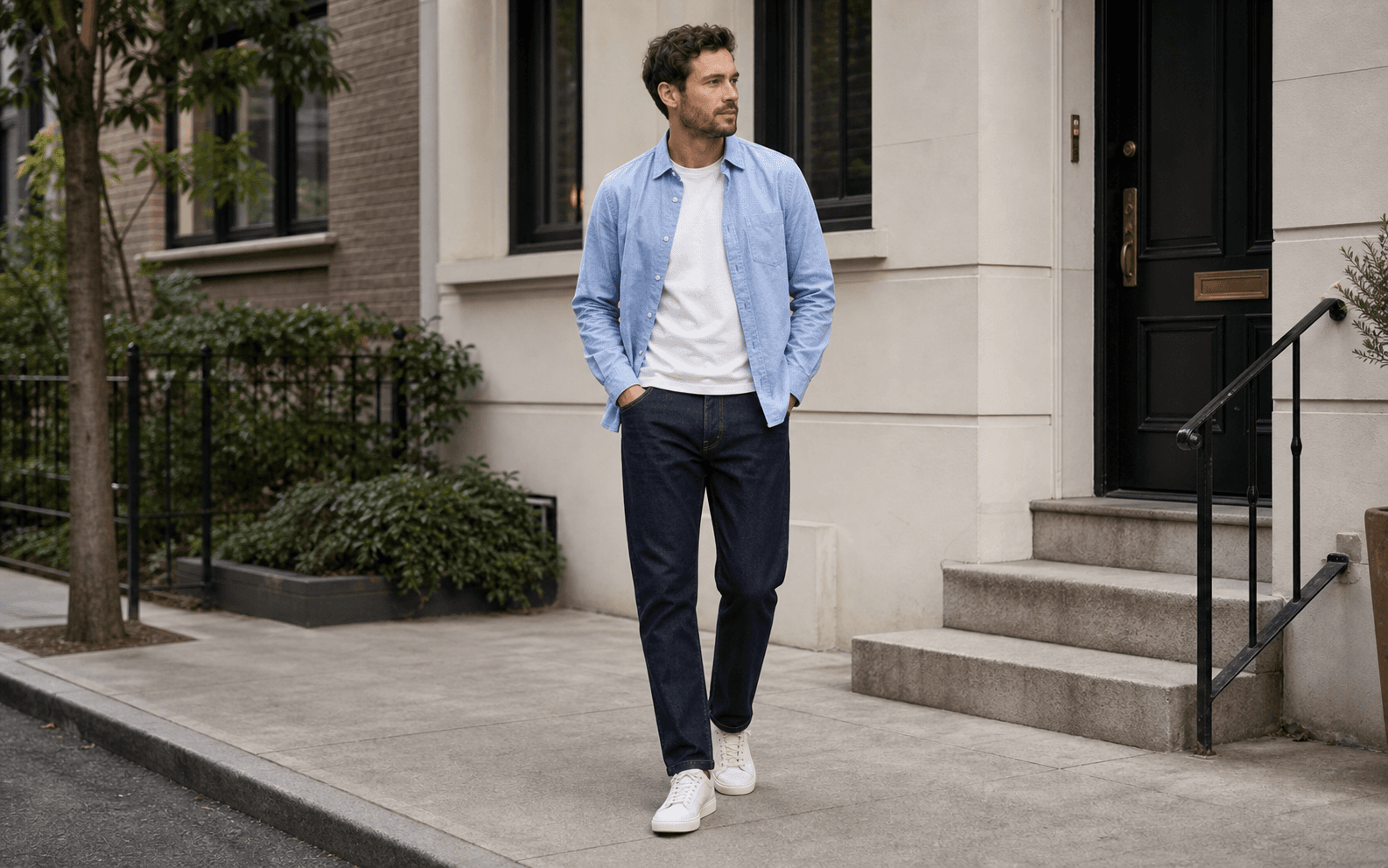 A man wearing a plain tee, open oxford shirt, dark jeans, and clean sneakers.