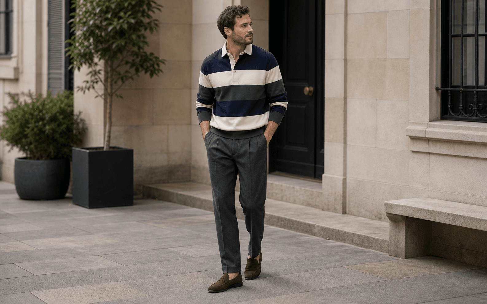 A man wearing a muted rugby shirt, tailored charcoal trousers, and brown loafers.