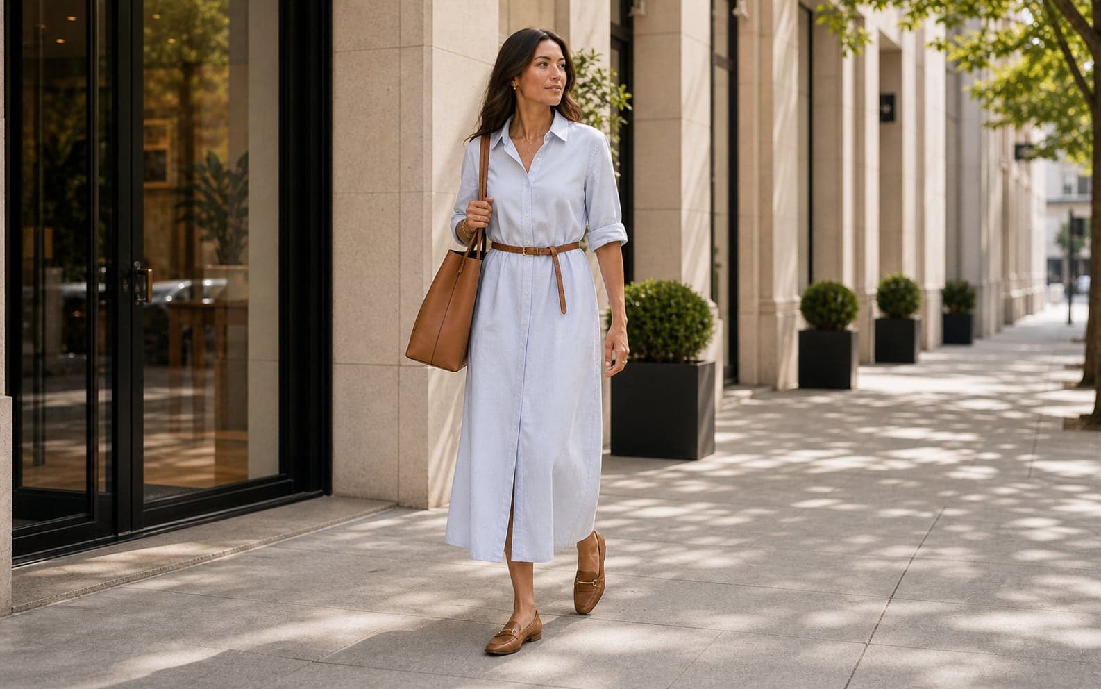 A woman wearing a pale shirt dress with a thin belt, tote, and flat summer office shoes.